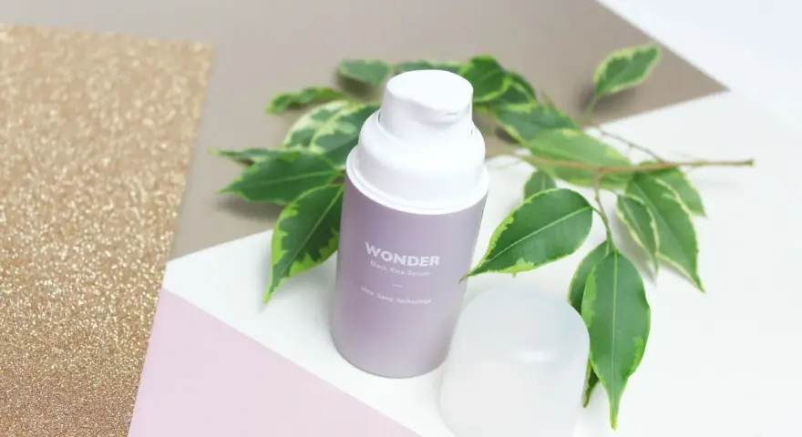 Wondeful! Serum z czarnego ryżu Haru Haru Wonder, otoczone zielonymi liśćmi, na tle błyszczącego złota i pastelowych kolorów.
