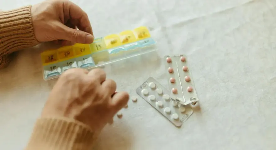 Dłonie układają tabletki w organizerze. Obok leżą blistry. Gdzie kupić tabletki antykoncepcyjne bez recepty?