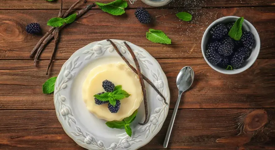 Budino fatto in casa alla vaniglia, guarnito con more fresche e menta. Ingredienti genuini per un dolce delizioso.