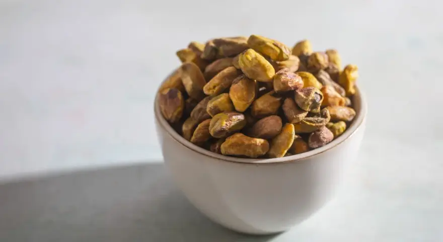 Misternie ułożone pistacje w miseczce. Czy pistacja to orzech? Botanicznie to pestkowiec, ale kulinarnie często traktowany jak orzech.