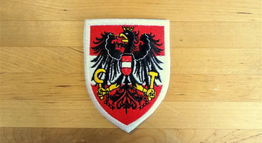 Naszywka z godłem Austrii: czarny orzeł z tarczą w biało-czerwone pasy, trzymający sierp i młot.