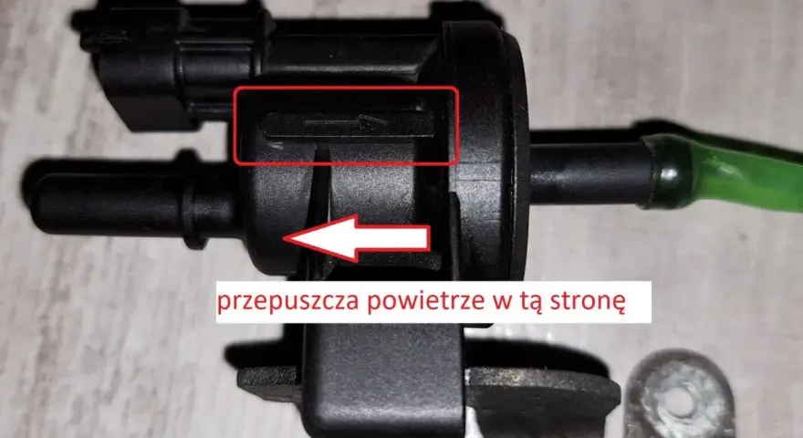 Zawór podciśnienia, potencjalna przyczyna błędu DTC P0170 w Volkswagen. Strzałka wskazuje kierunek przepływu powietrza.