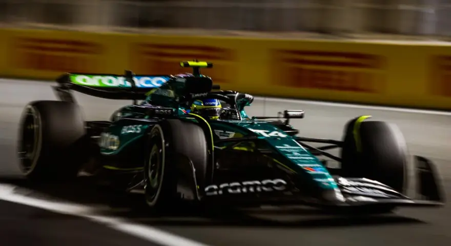 El Aston Martin AMR24 verde y negro acelera en la pista, con el piloto en su casco amarillo.