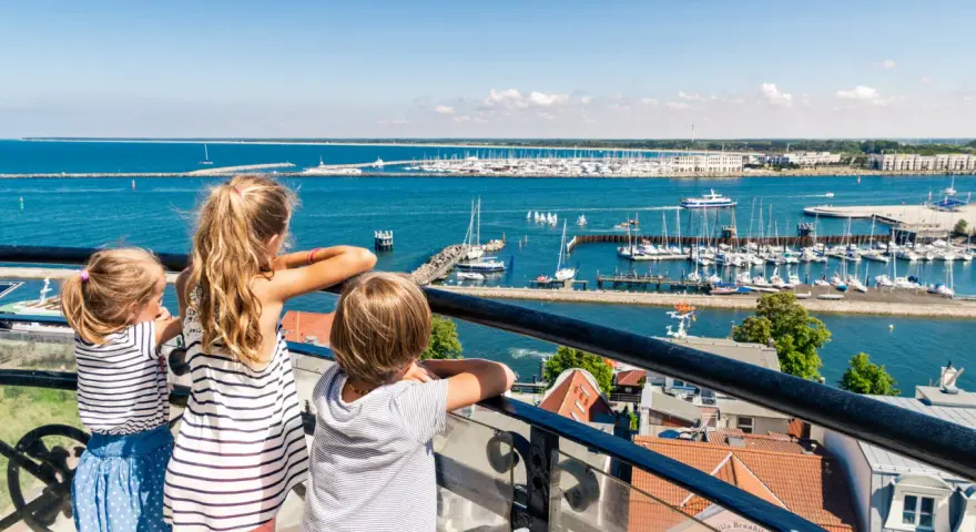 Drei Kinder blicken auf einen belebten Hafen mit vielen Segelbooten. Ein schöner Tag für Veranstaltungen MV mit Kindern.