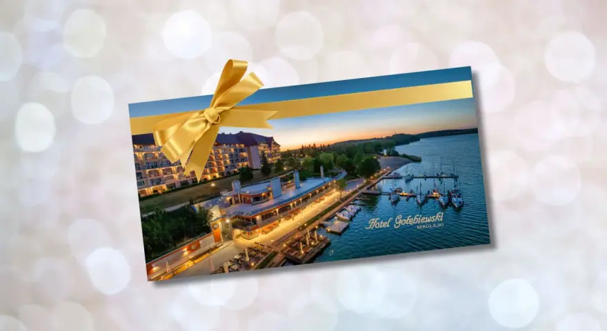 Złota karta Gołębiewski jak otrzymać? Voucher na pobyt w Hotelu Gołębiewski Mikołajki, ozdobiony złotą wstążką.