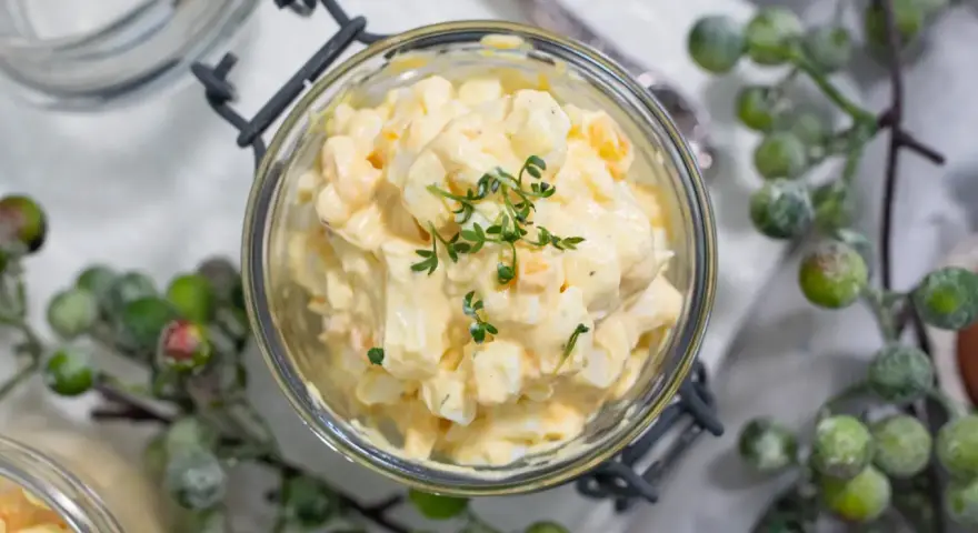 Cremiger Kartoffelsalat mit Fleischsalat, garniert mit frischen Kräutern, in einem Glas serviert.