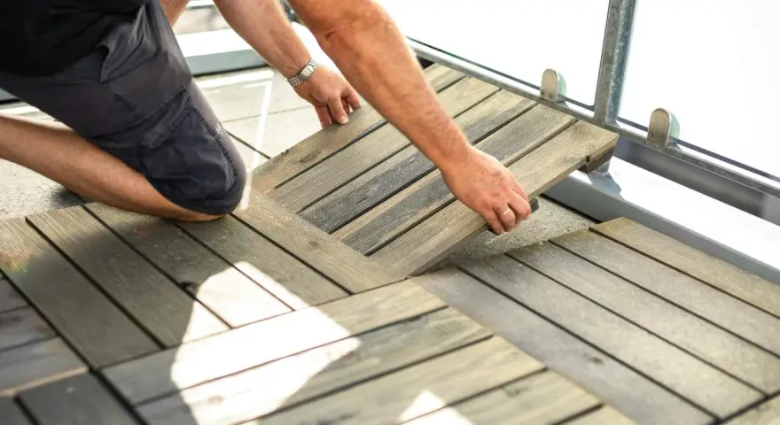 Mann legt Holzfliesen für den dachterrasse gestalten boden. Die Holzoptik passt gut zu modernen Außenbereichen.