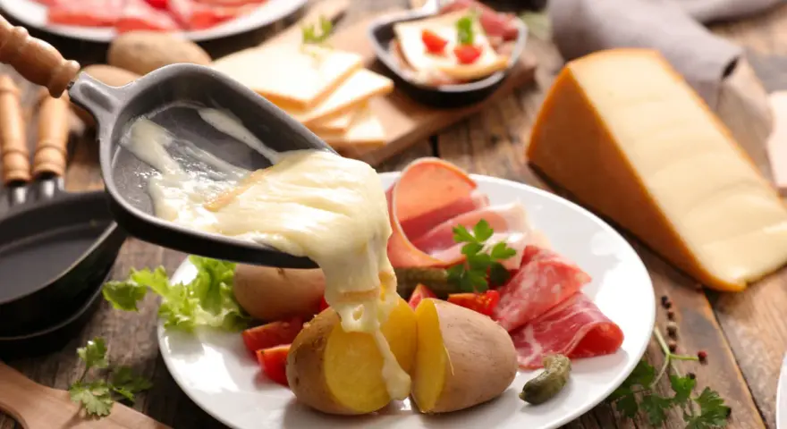 Roztopiony ser z patelni do raclette spływa na ziemniaki i wędliny. Pyszne danie raclette.
