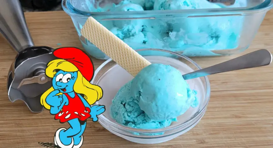 Schlumpfine genießt engelblaues Eis. Ein Handmixer und ein Waffelblatt liegen daneben.