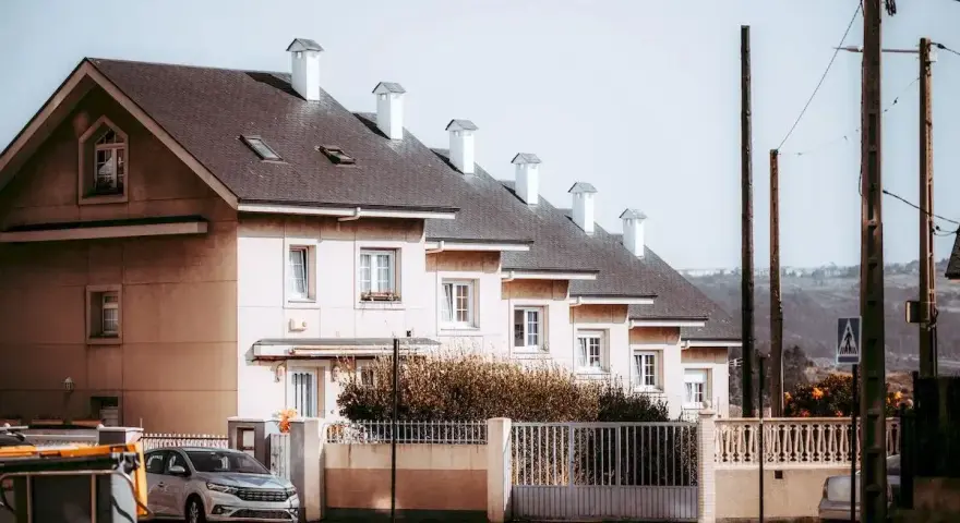 Rząd domów tworzy spójną zabudowę szeregową. Jasne fasady, ciemne dachy i białe kominy tworzą harmonijną całość.