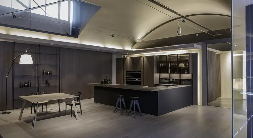 Moderna cocina office con isla central, muebles oscuros, estanterías y mesa de comedor.