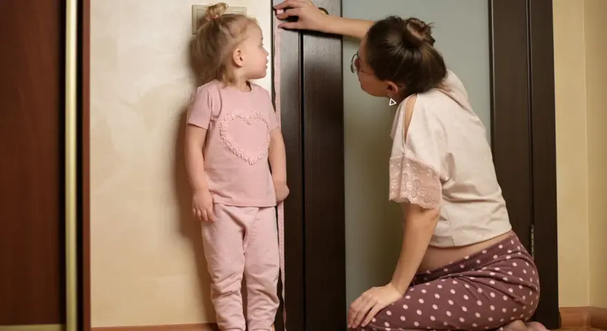 Mama mierzy wzrost dziecka przy drzwiach, sprawdzając, co na wzrost u dziecka.