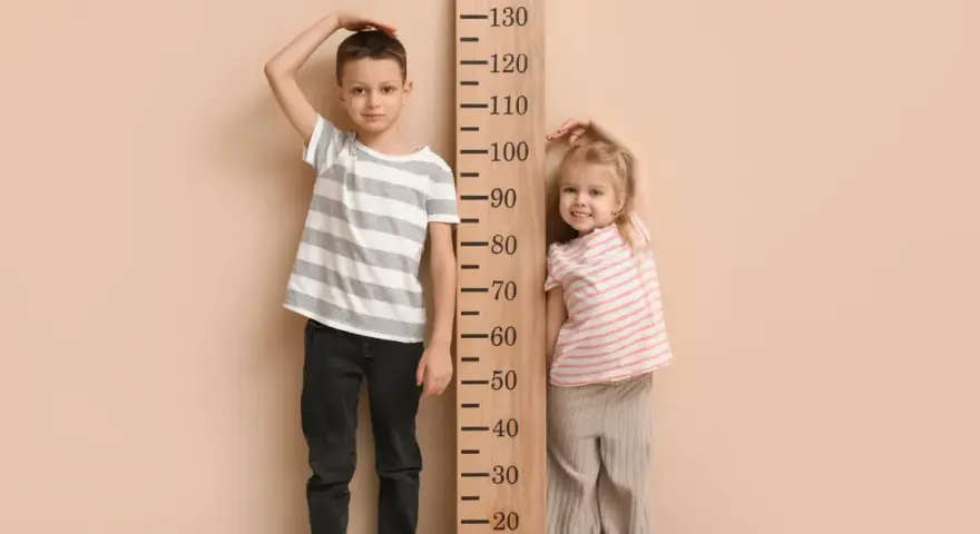Chłopiec i dziewczynka mierzą wzrost przy drewnianej miarce. Chłopiec ma ok. 110 cm, dziewczynka ok. 90 cm. Jaki rozmiar ubrań pasuje do ich wieku?