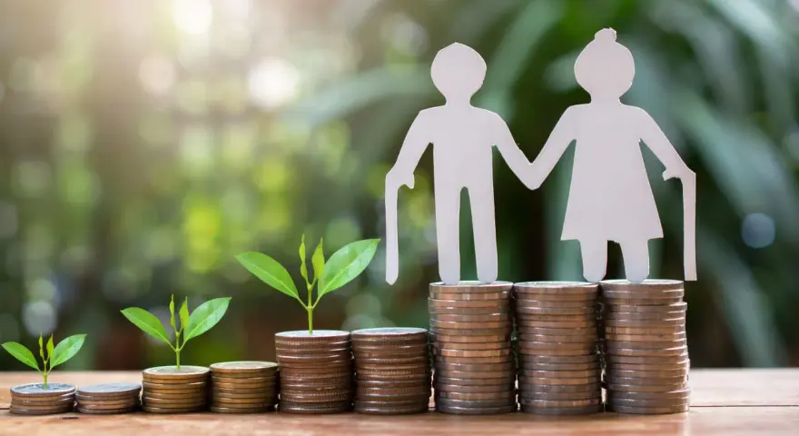 Figuras de papel de ancianos sobre pilas de monedas y brotes verdes. ¿Es sostenible el sistema de pensiones en España?