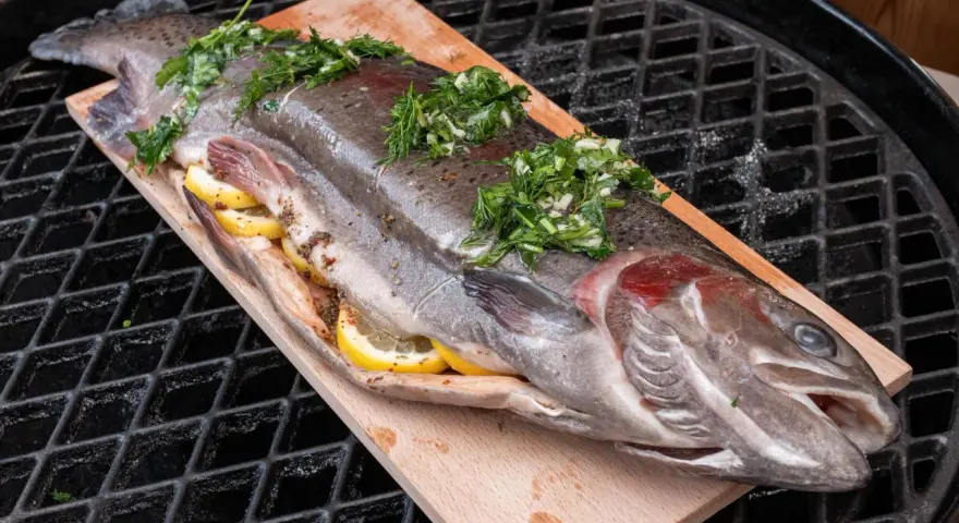 Lachsforelle auf einem Holzbrett, gefüllt mit Zitrone und Kräutern, bereit für den Grill. Die Kerntemperatur ist entscheidend für perfekten Fisch.