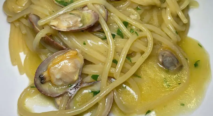 Spaghetti alle vongole cremosi come al ristorante, con vongole fresche e prezzemolo tritato su un letto di pasta dorata.
