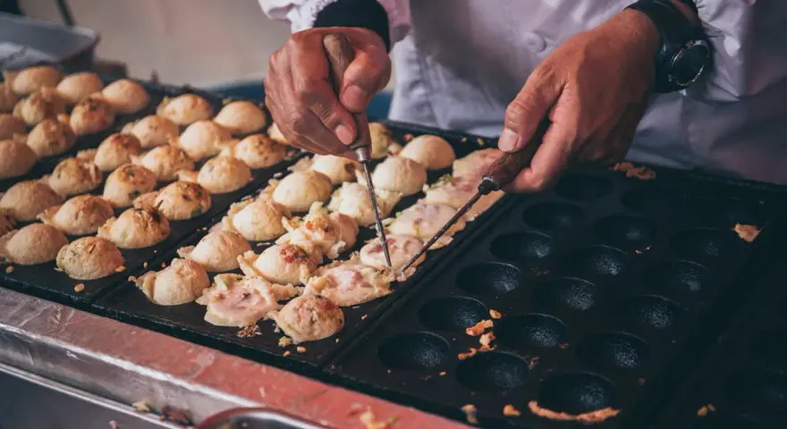 Ręce obracają kulki takoyaki na specjalnej patelni. Ten prosty takoyaki przepis jest w trakcie realizacji.