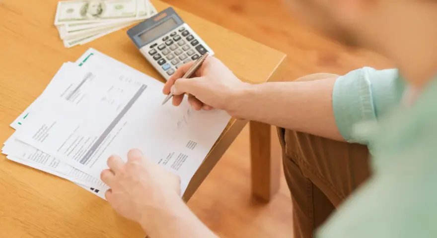 Persona revisa documentos y billetes, calculando cómo hacer un recibo de pago.