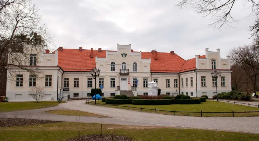 Pałac Przebendowskich w Wejherowie, z czerwonym dachem i kremową fasadą, otoczony zielenią i drzewami.