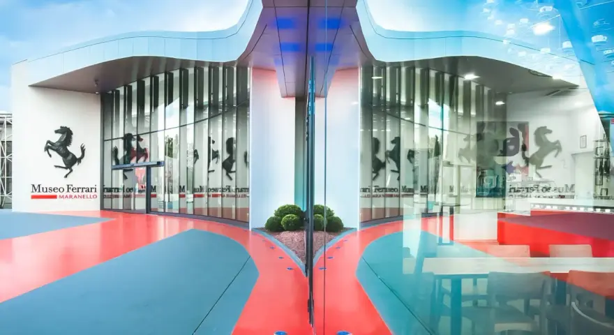Nowoczesne muzeum Ferrari w Maranello, z charakterystycznym logo i odbijającymi się w szkle sylwetkami koni.