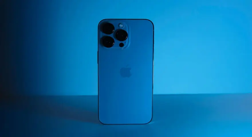 Elegancki iPhone 13 granatowy z potrójnym aparatem, lśniącym na tle niebieskiego światła.
