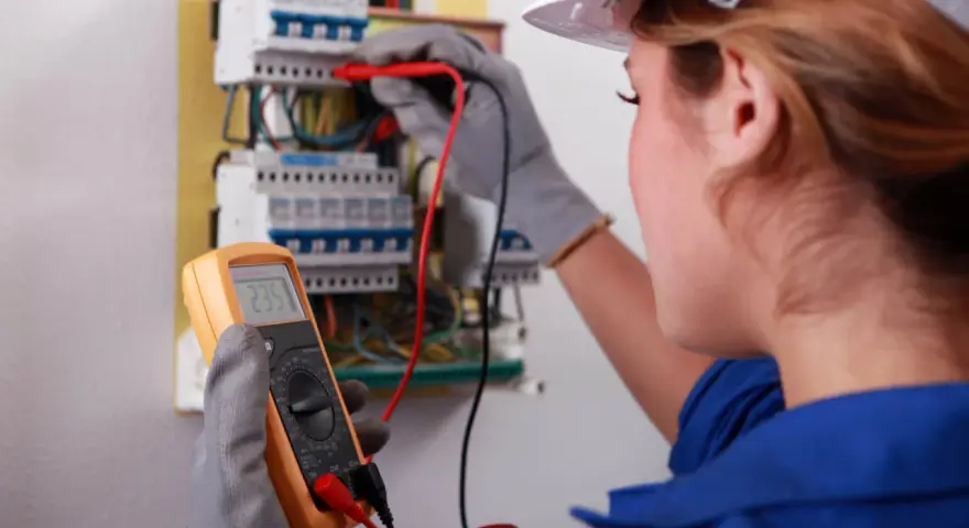 Elektryk wykonuje pomiary elektryczne w domu jednorodzinnym, używając multimetru do sprawdzenia instalacji.