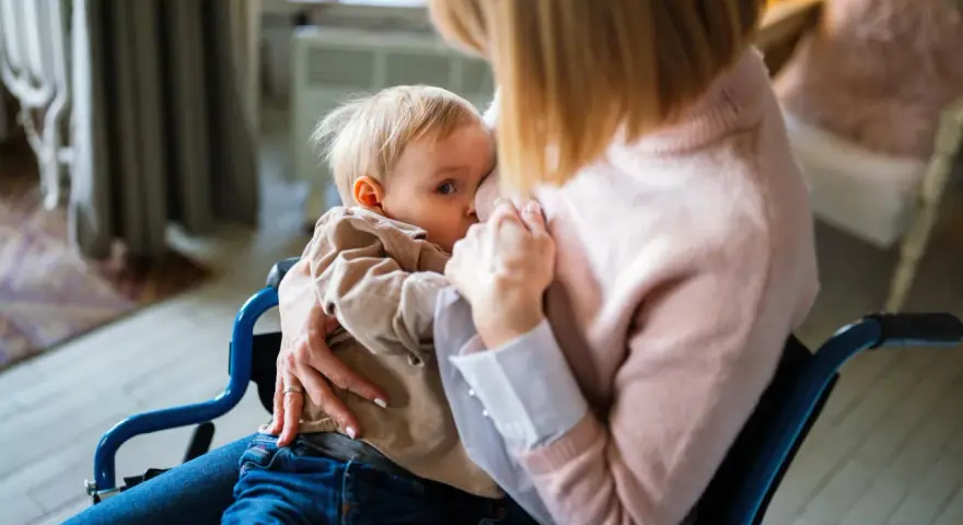 Mama w wózku inwalidzkim karmi piersią dziecko. To ważny moment, który może być częścią procesu, jak odstawić dziecko od piersi.