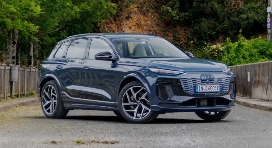 Elegancki, ciemnoniebieski Audi Q6 e-tron stoi na tle zieleni.