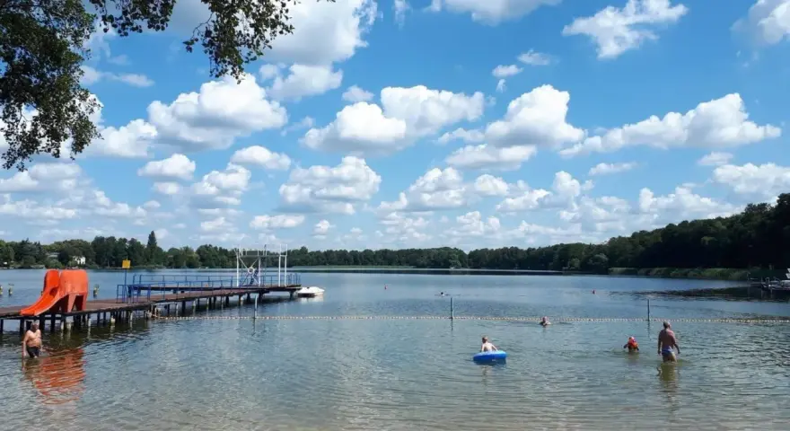Sommerfreude im Strandbad Heiligensee: Kinder planschen, ein Mann kühlt sich ab, eine Rutsche lockt. Blauer Himmel mit weißen Wolken.