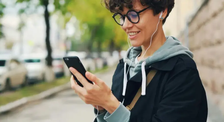 Uśmiechnięta osoba w słuchawkach patrzy na telefon. Czy wiesz, co to jest impedancja w słuchawkach i jak wpływa na dźwięk?