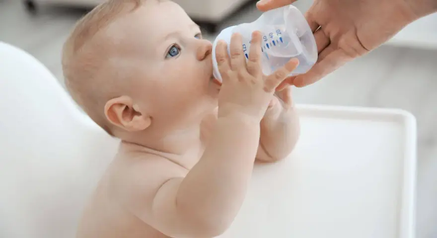 Niemowlę pije wodę z butelki. To idealne co do picia dla niemowlaka, gdy jest spragnione.