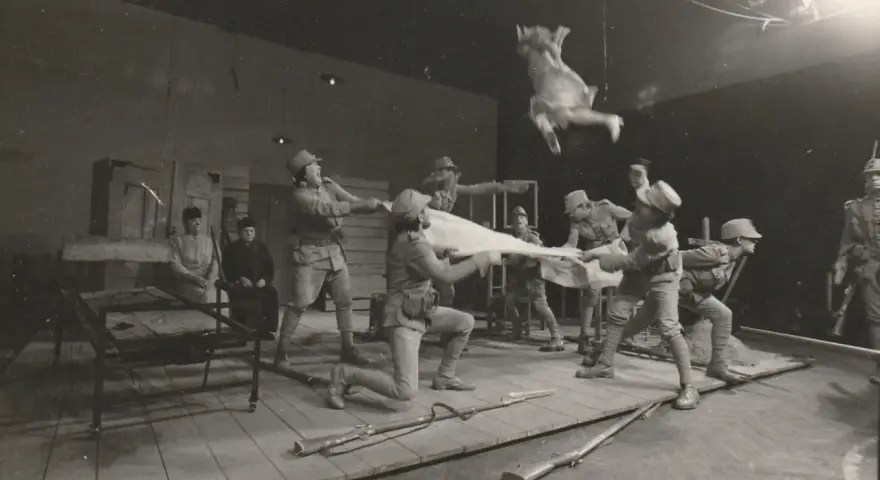 Scena teatralna: żołnierze w mundurach z epoki, jeden w powietrzu, trzymają białą tkaninę. Kantor Wielopole.