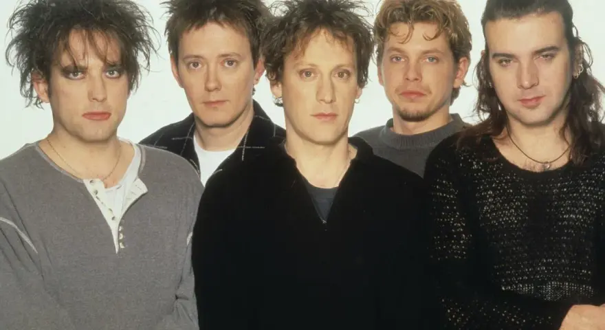 The Cure członkowie w szarych i czarnych ubraniach, z charakterystycznymi fryzurami i makijażem.