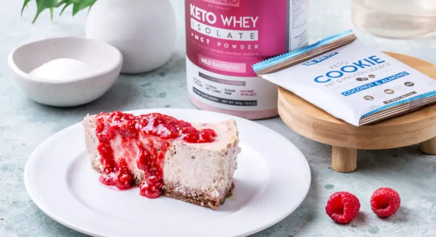 Pyszny sernik keto z malinami, obok słoik Keto Whey Isolate i batonik Keto Cookie. Idealny keto spod do sernika.
