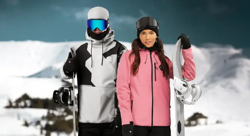 Pareja con tablas de snowboard, ella con chaqueta rosa, él con chaqueta gris y negra. Opiniones sobre Sorona Aura: ¡calidez y estilo en la montaña!