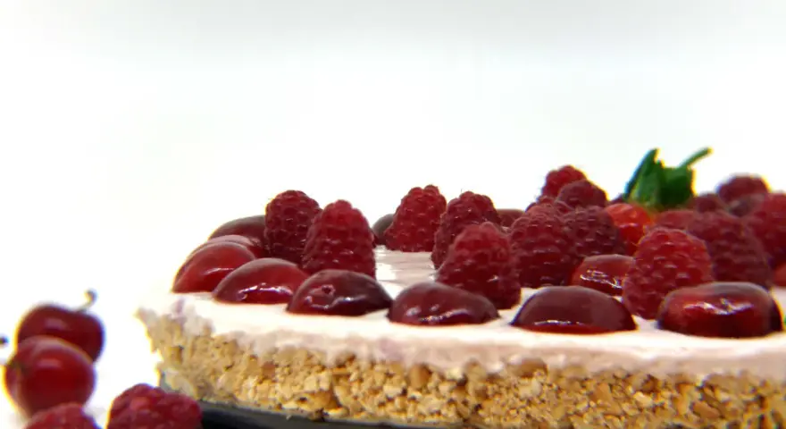 Cheesecake senza gelatina, guarnita con lamponi succosi e ciliegie lucide, su una base croccante.