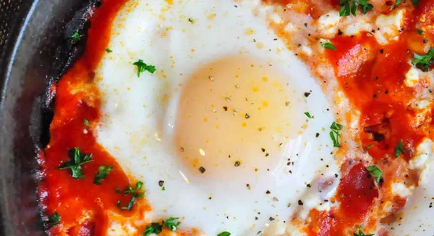 Uova al pomodoro, un piatto saporito con uovo cotto in salsa di pomodoro e formaggio, guarnito con prezzemolo fresco.