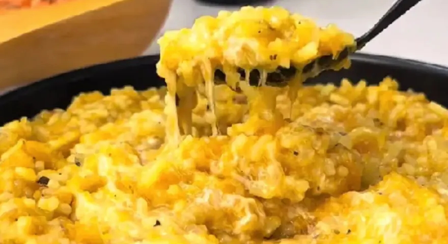 Risotto cremoso de calabaza en un plato, con una cuchara sacando una porción.