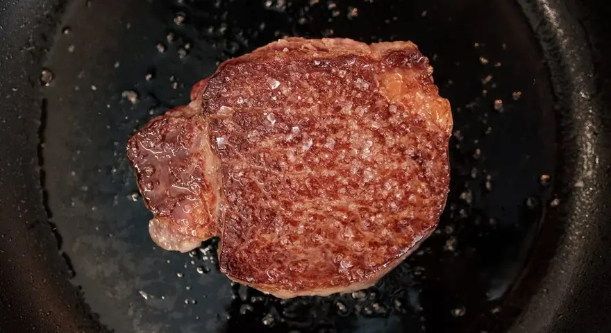 Ein saftiges Steak brutzelt in der Pfanne, bestreut mit grobem Salz.