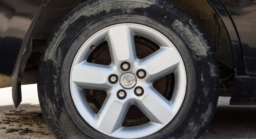 Ruota sgonfia dell'auto, con cerchione in lega a cinque razze e pneumatico sporco.