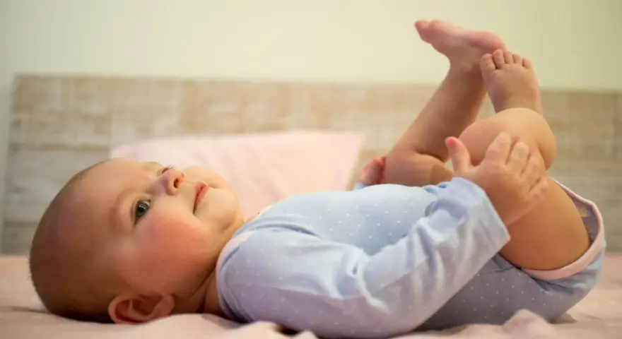 Uśmiechnięte, 5 miesięczne dziecko leży na plecach, podnosząc nóżki do góry.