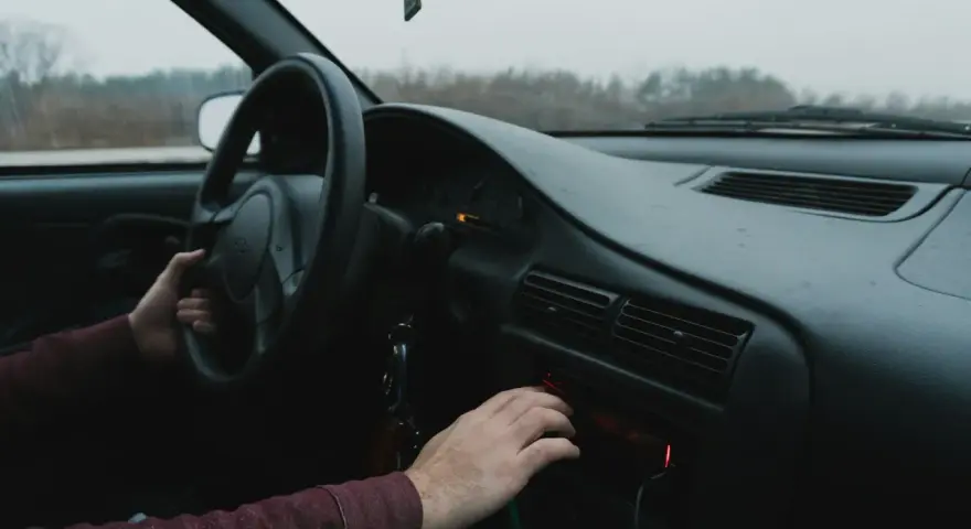 Dłoń kierowcy reguluje radio samochodowe.