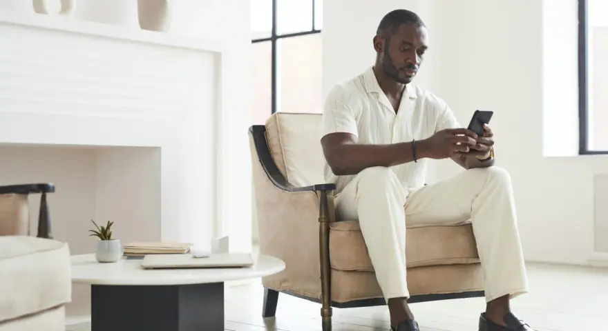 Un homme en tenue claire, assis dans un fauteuil, regarde son téléphone. Il attend un message, car il ne m'écrit plus comme avant.
