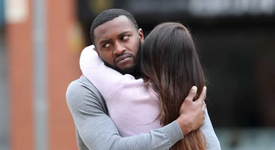 Un homme étreint une femme, mais son regard trahit des signes qu'il parle à une autre.