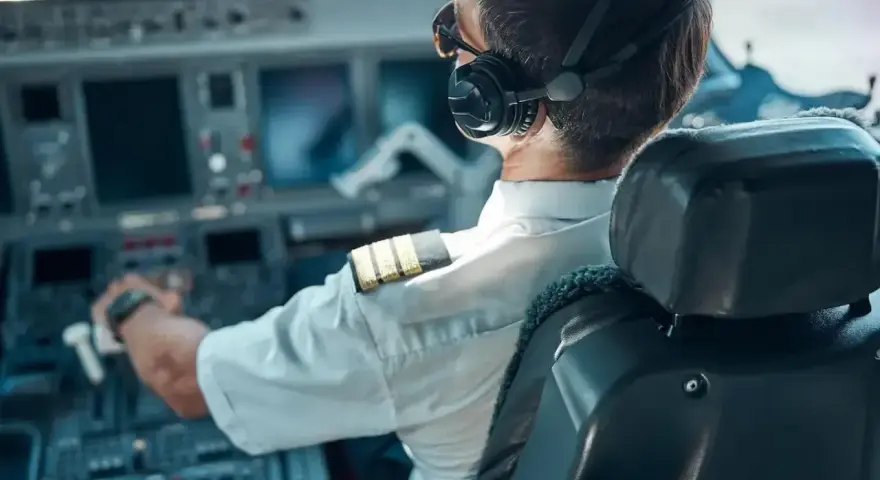 Pilot samolotu w słuchawkach i okularach przeciwsłonecznych, siedzący w kokpicie.