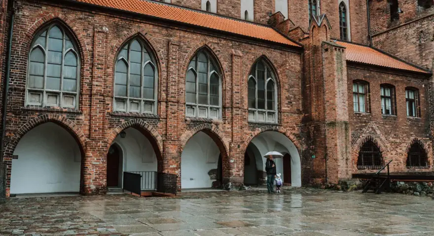 Zamek w Kwidzynie zaprasza. W deszczowy dzień zwiedzający z parasolem podziwiają gotycką architekturę. Bilety dostępne online.