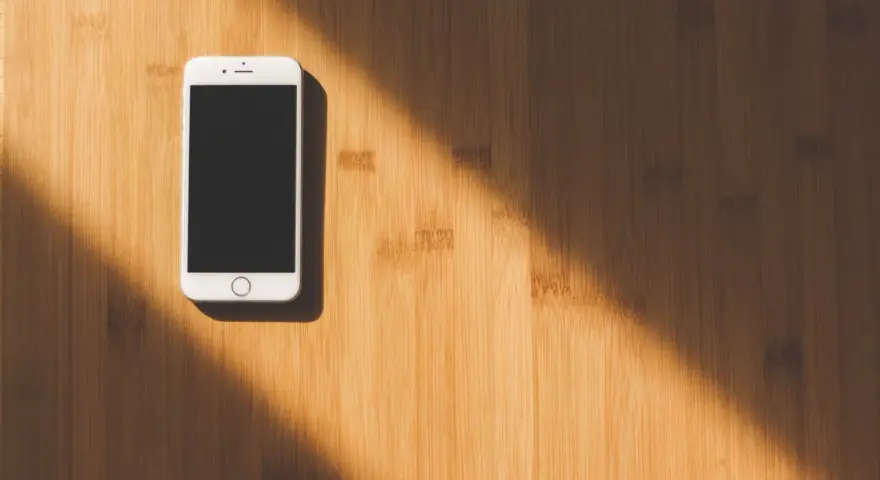 Biały smartfon leży na drewnianym blacie. Słońce rzuca cień. Jak namierzyć telefon, gdy zaginie?