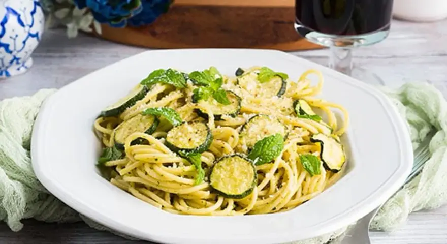 Un piatto di pasta e zucchine alla siciliana, guarnito con menta fresca e parmigiano.
