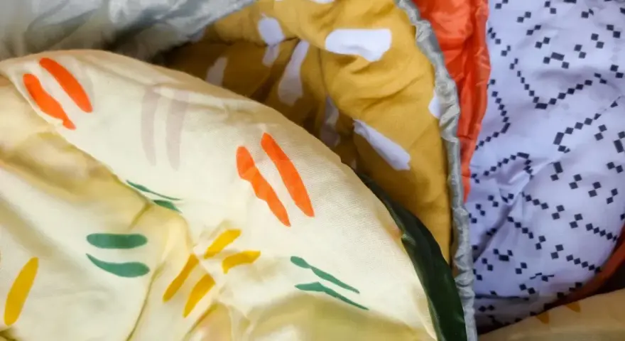 Bunte Muster auf einem Schlafsack aus Baumwolle oder Polyester. Ein gelber Stoff mit orangen und grünen Streifen, daneben ein orangefarbener und ein weißer Stoff mit schwarzen Punkten.