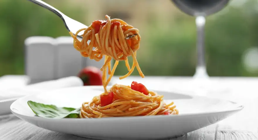 Widok na talerz spaghetti z sosem pomidorowym i listkiem bazylii. Widelec podnosi porcję makaronu. Idealne pytanie: jakie wino do bolognese?